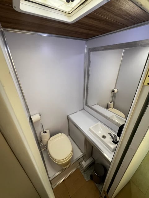 Compact RV bathroom interior with toilet on left and small sink with mirror on right, skylight above