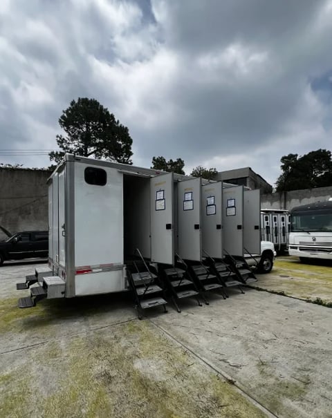 White mobile restroom trailer with extended entry stairs parked on pavement, overcast sky, industrial facility setting