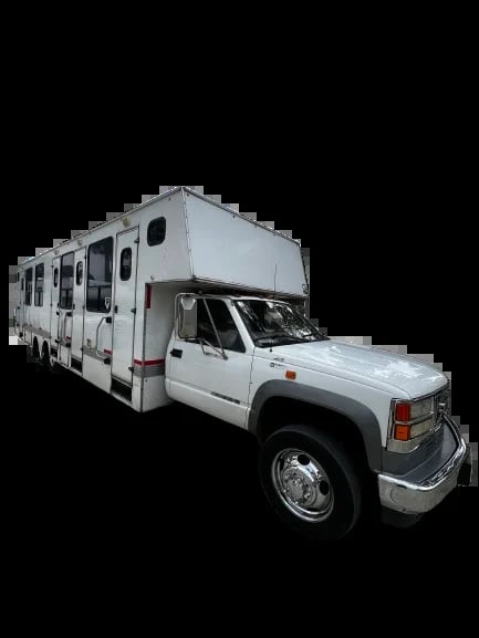 White motorhome RV with cab-over sleeping quarters built on truck chassis, shown against black background