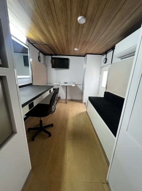 Modern interior of a compact office trailer or mobile workspace with wooden ceiling, desk, chair, and seating area