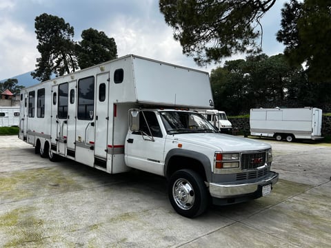 White motorhome built on a GMC pickup truck chassis parked outdoors with trees in background