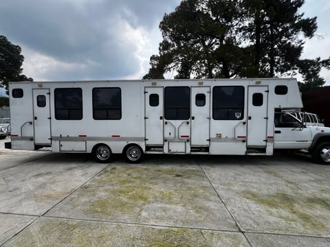 White horse trailer with aluminum exterior parked on concrete surface with trees in background