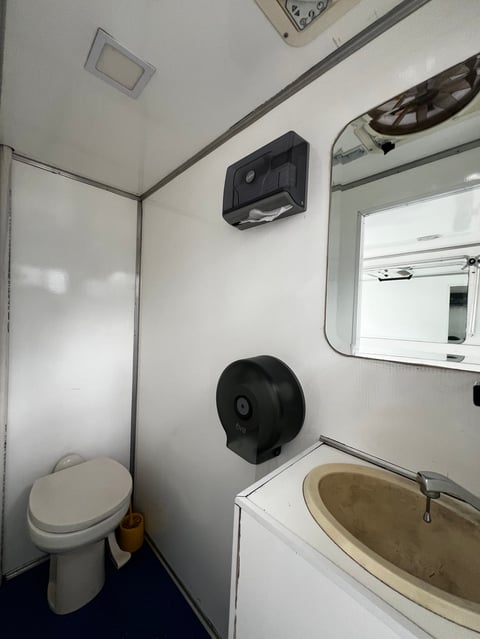 Compact portable toilet interior with toilet, sink, mirror, paper towel dispenser, and wall-mounted fixtures