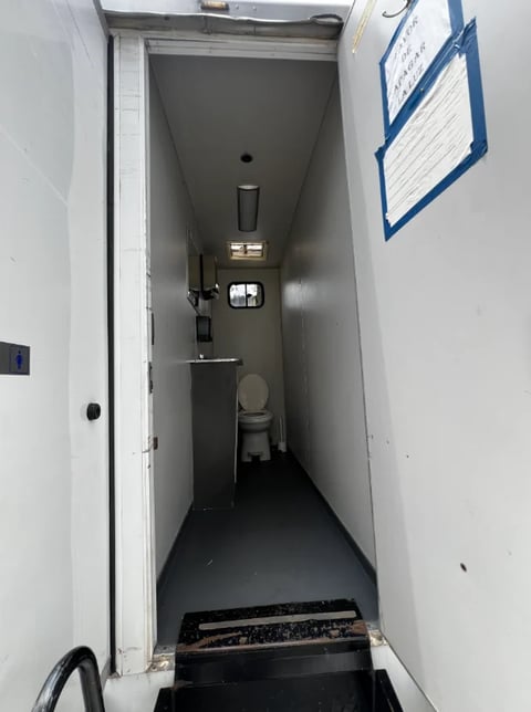 Interior view of narrow bathroom with toilet, sink, and utility notices on walls