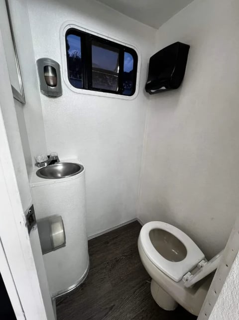 Modern portable bathroom stall with white walls, toilet, sink, digital display panel, and dark wood flooring