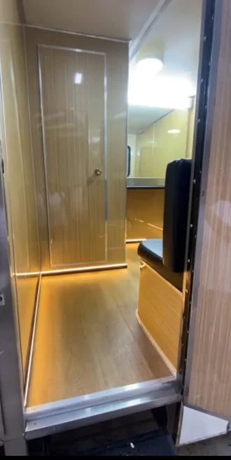 Modern glass shower enclosure with chrome frame and warm lighting reflecting off wooden flooring