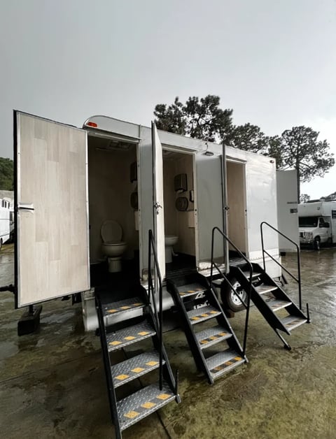Multiple portable restroom trailers with metal stairs and handrails parked outdoors on wet pavement
