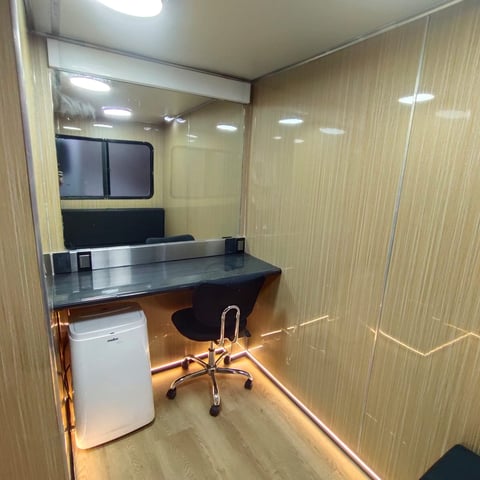 Small office space with desk, black office chair, white trash can, and glass partition wall dividing the room
