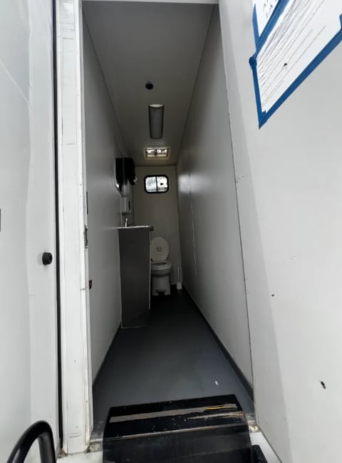 Narrow bathroom or utility room corridor with dark floor, white walls, sink, and toilet visible at far end