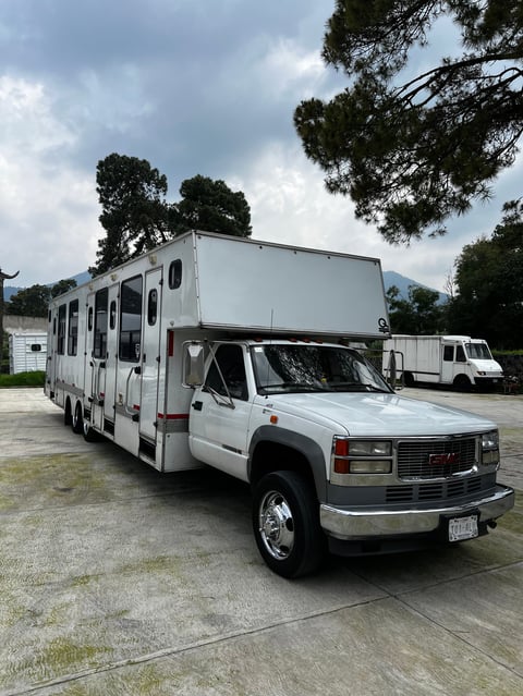 White class C motorhome built on pickup truck chassis parked in lot with trees in background