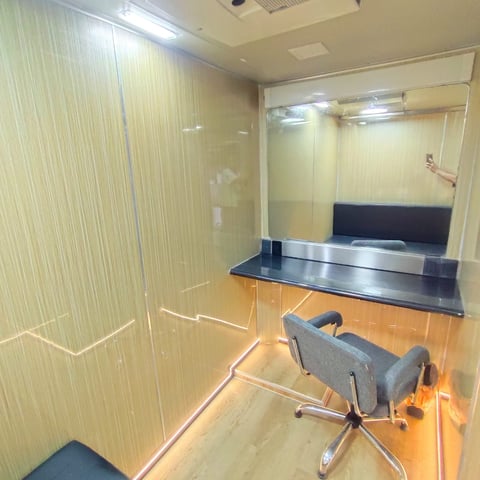Small office room with glass partition walls, black desk, gray office chair, and warm wooden flooring