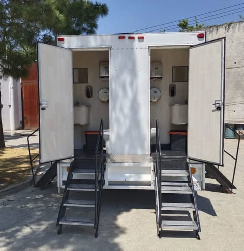 Two white portable toilet units side by side with metal stairs and open doors, showing interior fixtures