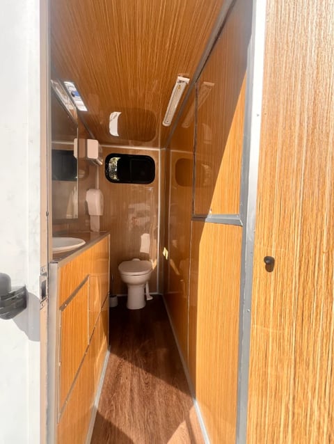 Interior of an RV bathroom featuring wood paneling, toilet, sink, and shower area with chrome fixtures