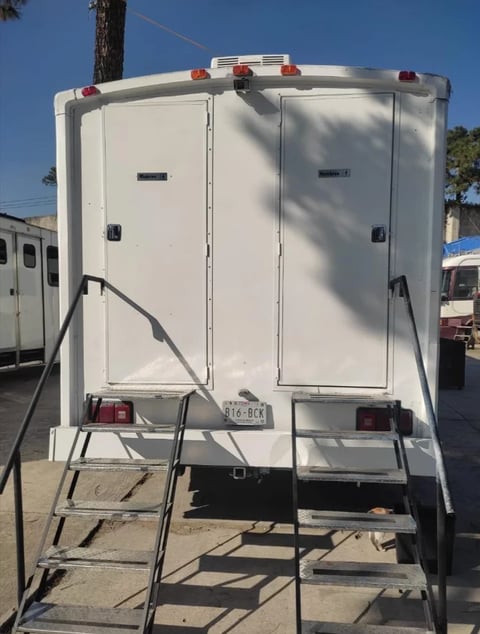 White travel trailer viewed from rear, showing double doors, red tail lights, and metal step ladder in an outdoor lot