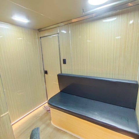 Interior of a luxury trailer with light wood paneling, a black leather bench seat, and a glass shower enclosure with metal frame.