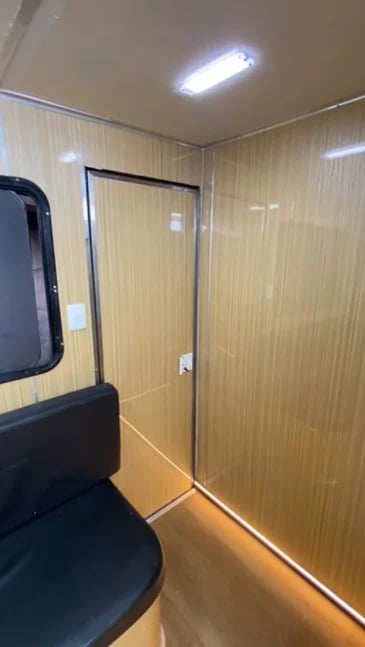 Interior of a compact travel trailer with wood-grain paneled walls, LED ceiling lights, and an open doorway