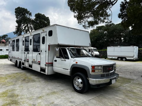 White commercial truck with extended RV cabin parked in lot with trees and buildings in background