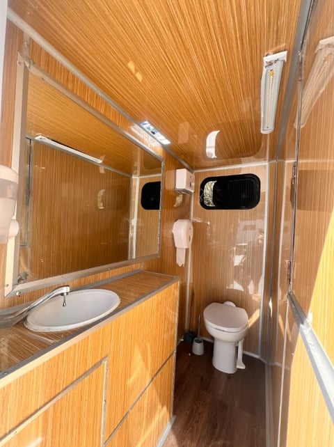 Interior of a portable restroom trailer with wood paneling, sink, mirror, and toilet