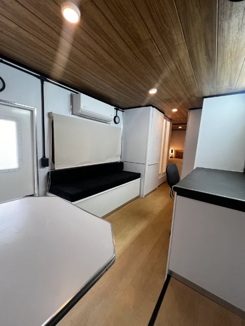 Interior of a modern RV with wood ceiling, white cabinetry, black mattresses on bunks, and wooden flooring