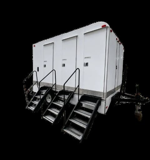White portable restroom trailer with three stalls, black metal stairs, and wheels on black background