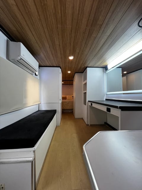 Interior of modern RV with wood ceiling, white cabinetry, built-in furniture, and hardwood flooring