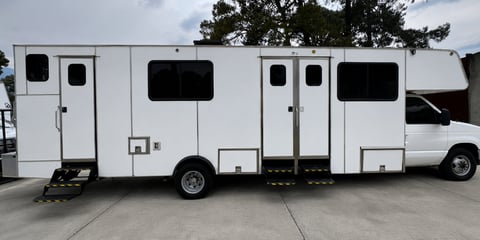 White recreational vehicle parked on concrete with entry door, windows, and tinted sections visible on its side