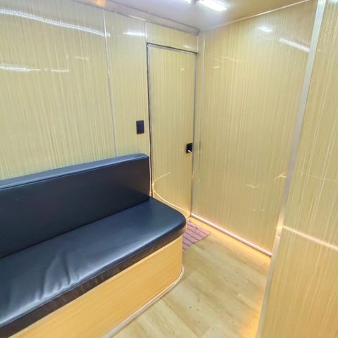 Interior of a small modern booth or cabin with wood paneling, a dark blue cushioned bench seat on the left, glass doors, and LED lighting