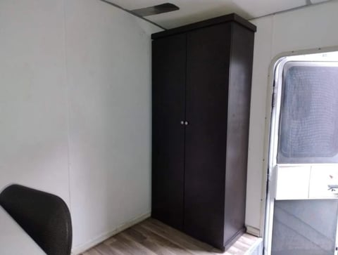 Black wardrobe cabinet in small room with white walls, chair, and window with blind