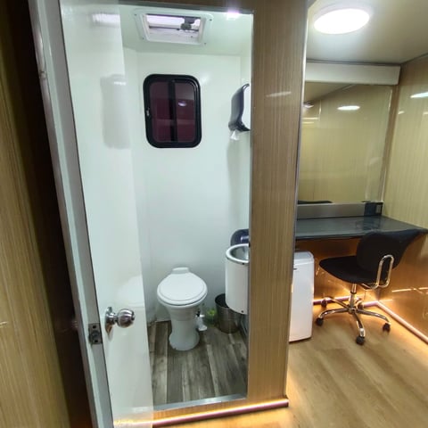 Compact bathroom with toilet and sink inside a small office or mobile space with desk area visible